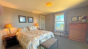 Une chambre à coucher avec un lit, des lampes de chevet, une commode, un banc et une fenêtre donnant sur un beau paysage.