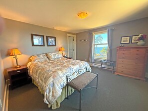 A bedroom with a bed, bedside lamps, a dresser, a bench, and a window with a view.