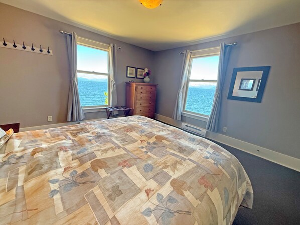 A bedroom with a large bed, two windows with curtains, a dresser, and a wall-mounted light fixture.