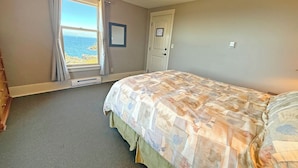 Une chambre à coucher avec un lit, une fenêtre donnant sur la mer, une porte et un thermostat fixé au mur.