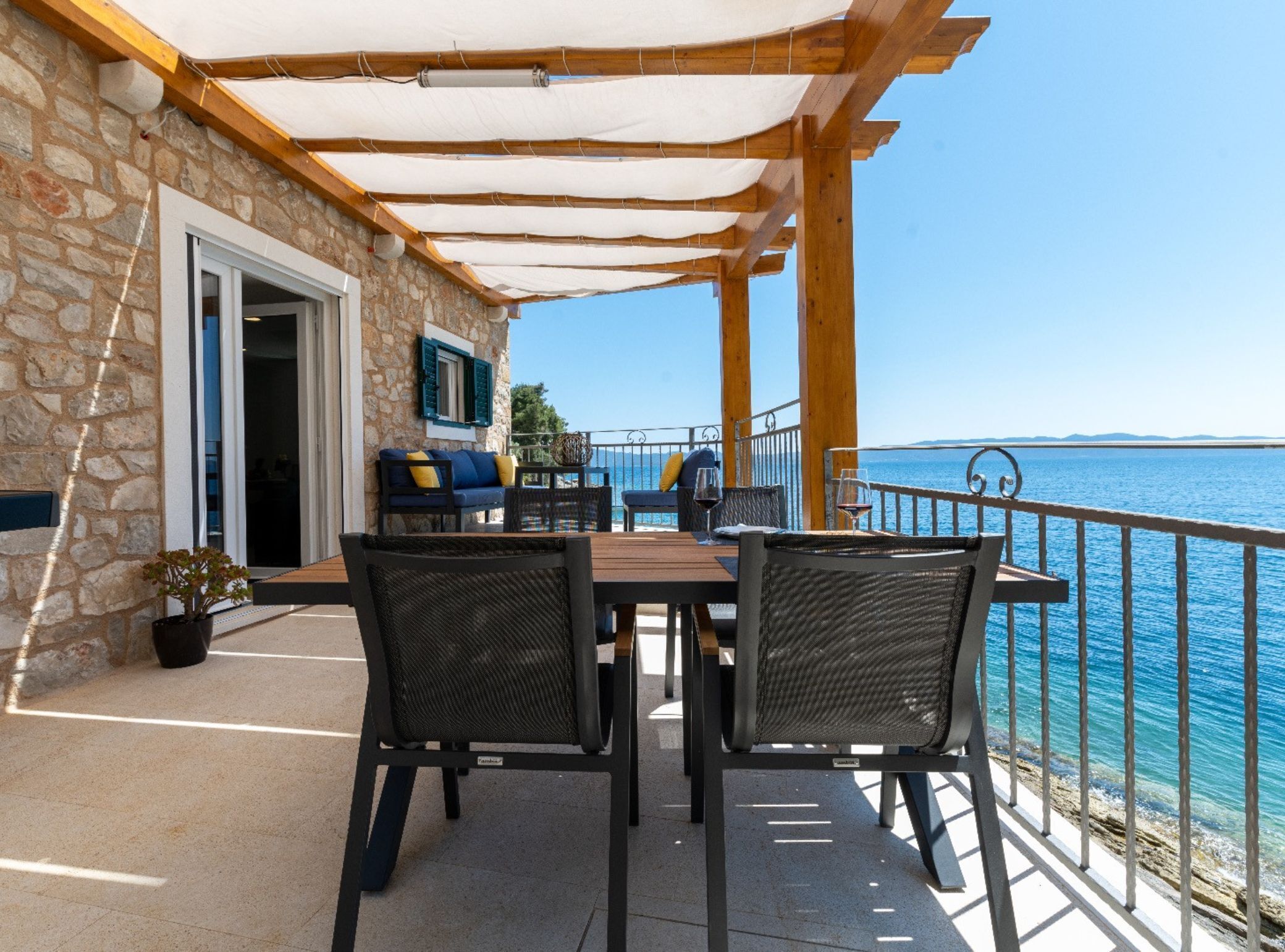 A stone building with a wooden deck, outdoor seating, and a view of the sea.