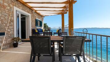 A stone building with a wooden deck, outdoor seating, and a view of the sea.