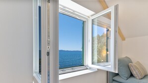 A room with a large window offering a view of the sea, a sofa with cushions, and a floor lamp.