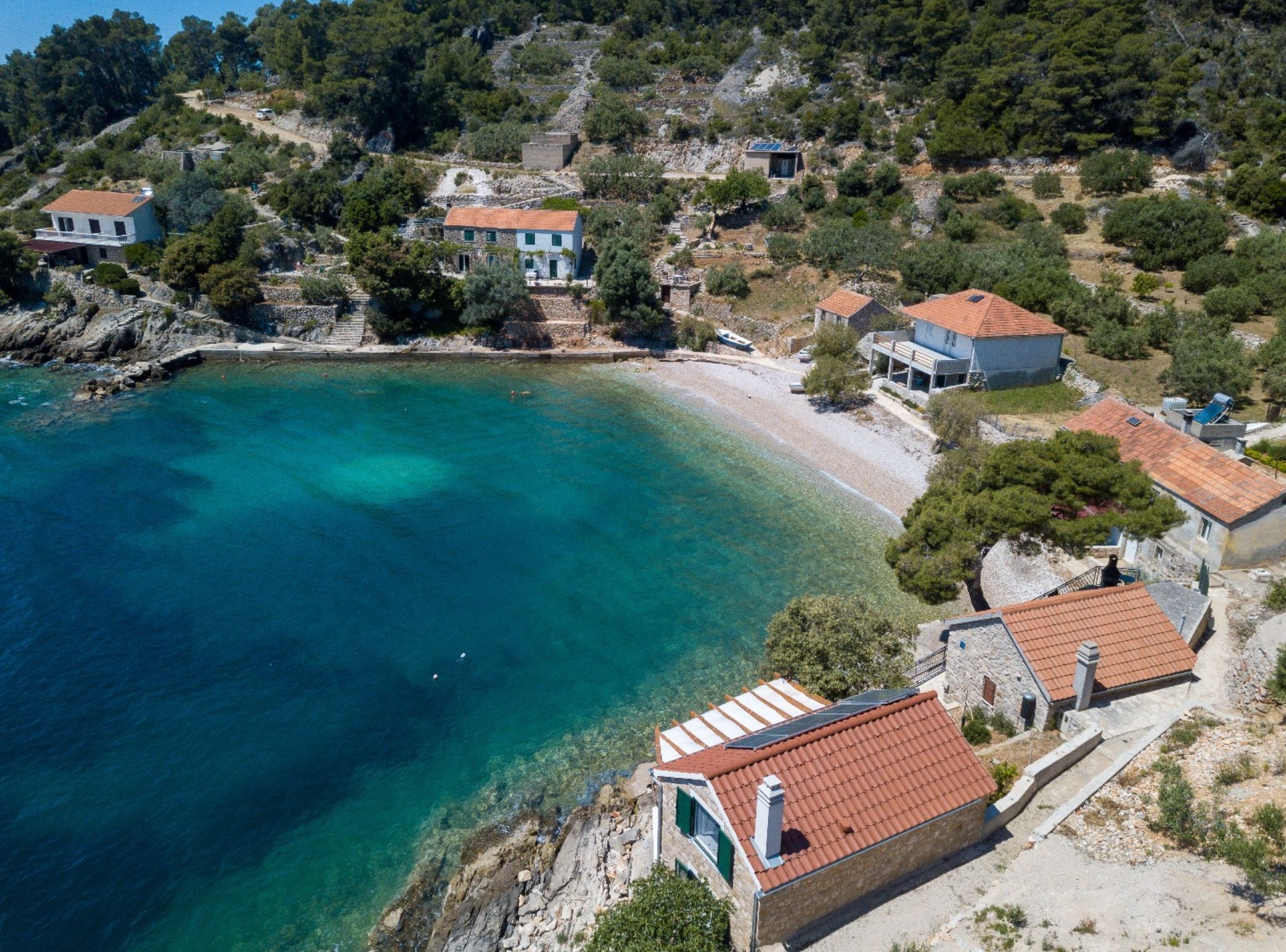 An aerial view of a coastal area with houses, clear turquoise waters, and a rocky shoreline.