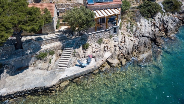 A coastal property with a stone staircase leading to a wooden deck, a building with a solar panel, and clear blue water.