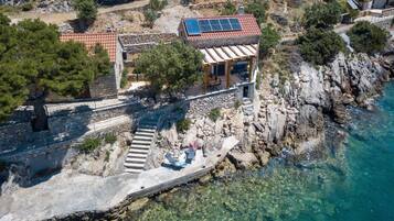 A coastal property with a stone staircase leading to a wooden deck, a building with a solar panel, and clear blue water.