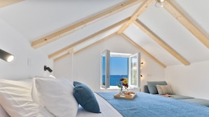 A bedroom with a bed, pillows, a bedside table with a lamp, a window with a view, and a small table with a tray.