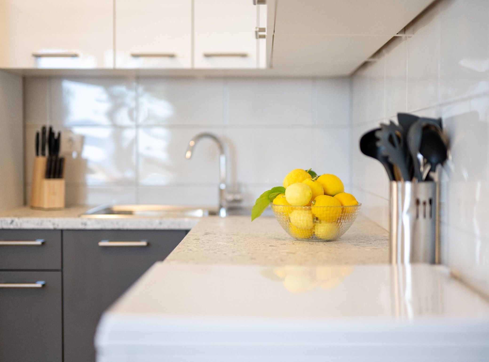 A kitchen with a bowl of lemons on the counter, a knife block, and a modern faucet.