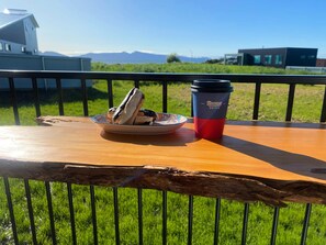 Ein Holztisch mit einer Speisenplatte und einer Kaffeetasse, vor einer Kulisse aus grünem Gras und fernen Bergen.