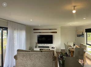 Ein Wohnzimmer mit einer Couch, einem Esstisch, Stühlen, einem Flachbildfernseher und zwei Holzschlägern an der Wand.