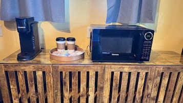 A coffee maker, a microwave, and a tray with coffee cups on a wooden counter.