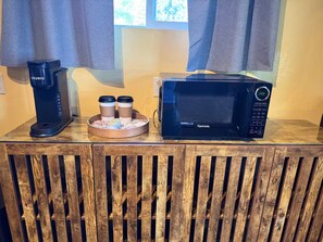 Eine Kaffeemaschine, eine Mikrowelle und ein Tablett mit Kaffeetassen auf einer Holzauslage.