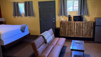 A room with a bed, a sofa, a small table, a microwave, and a TV on a wooden cabinet.