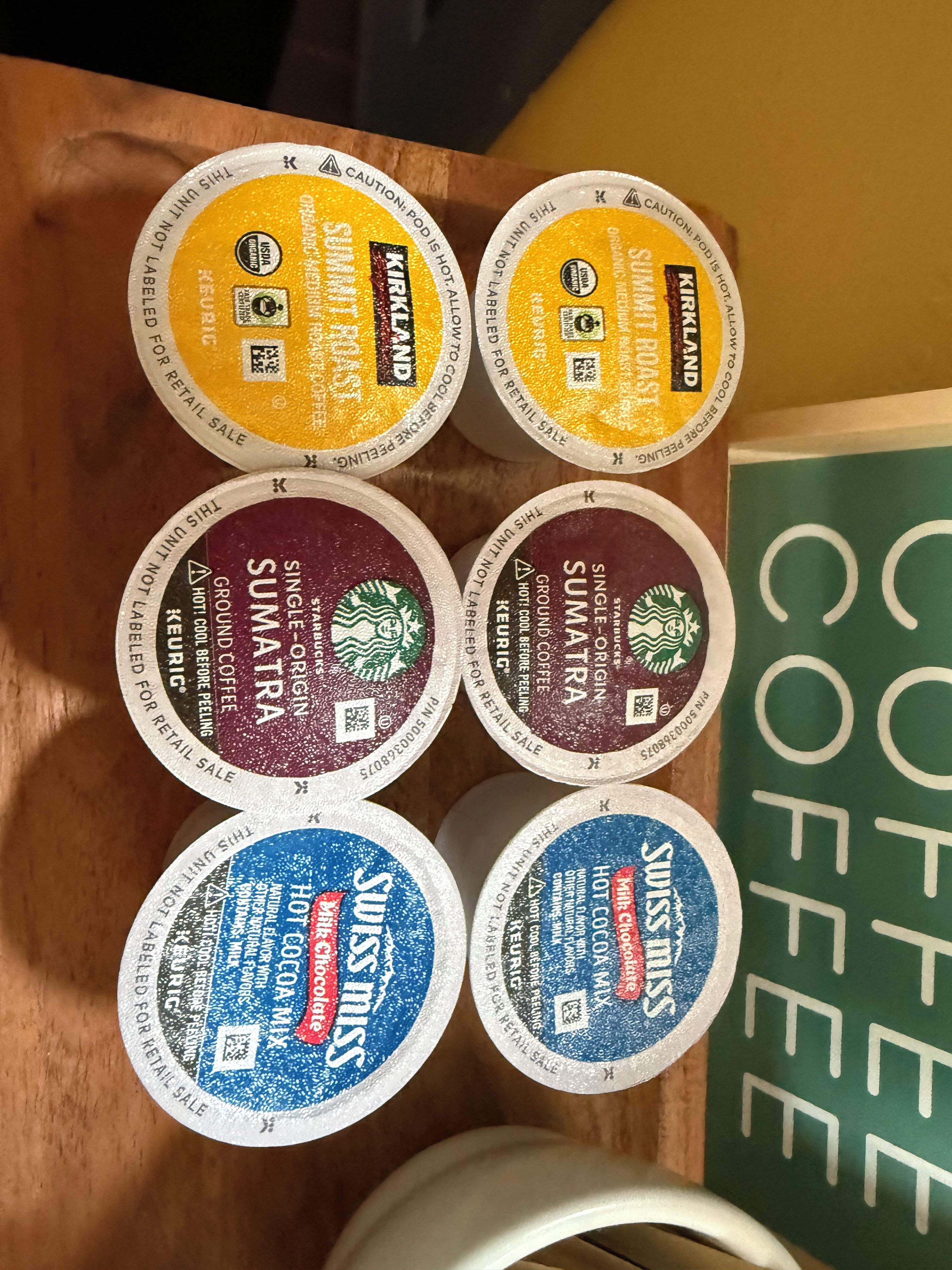 Zes koffiekapsules gerangschikt op een houten ondergrond, elk met een ander etiket dat de koffiesoort aangeeft.