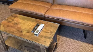 A brown leather sofa with a blanket, a wooden coffee table with a remote control, and a carpeted floor.
