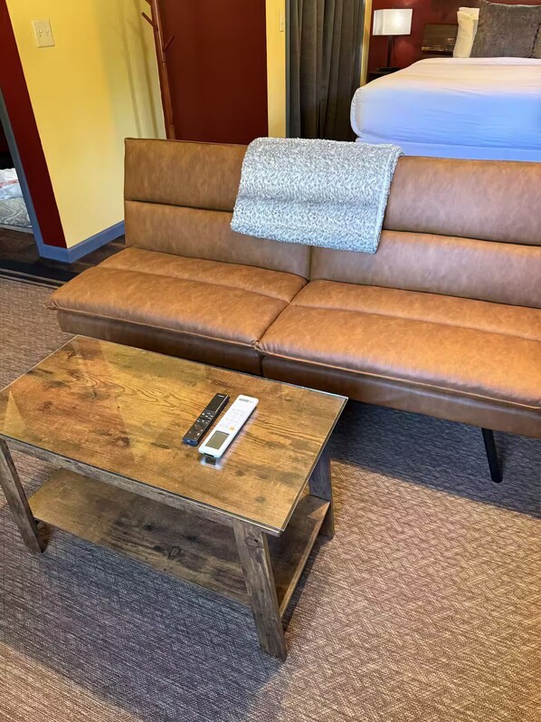 Ein braunes Ledersofa mit einer Decke, ein Couchtisch aus Holz mit einer Fernbedienung und ein Teppichboden.