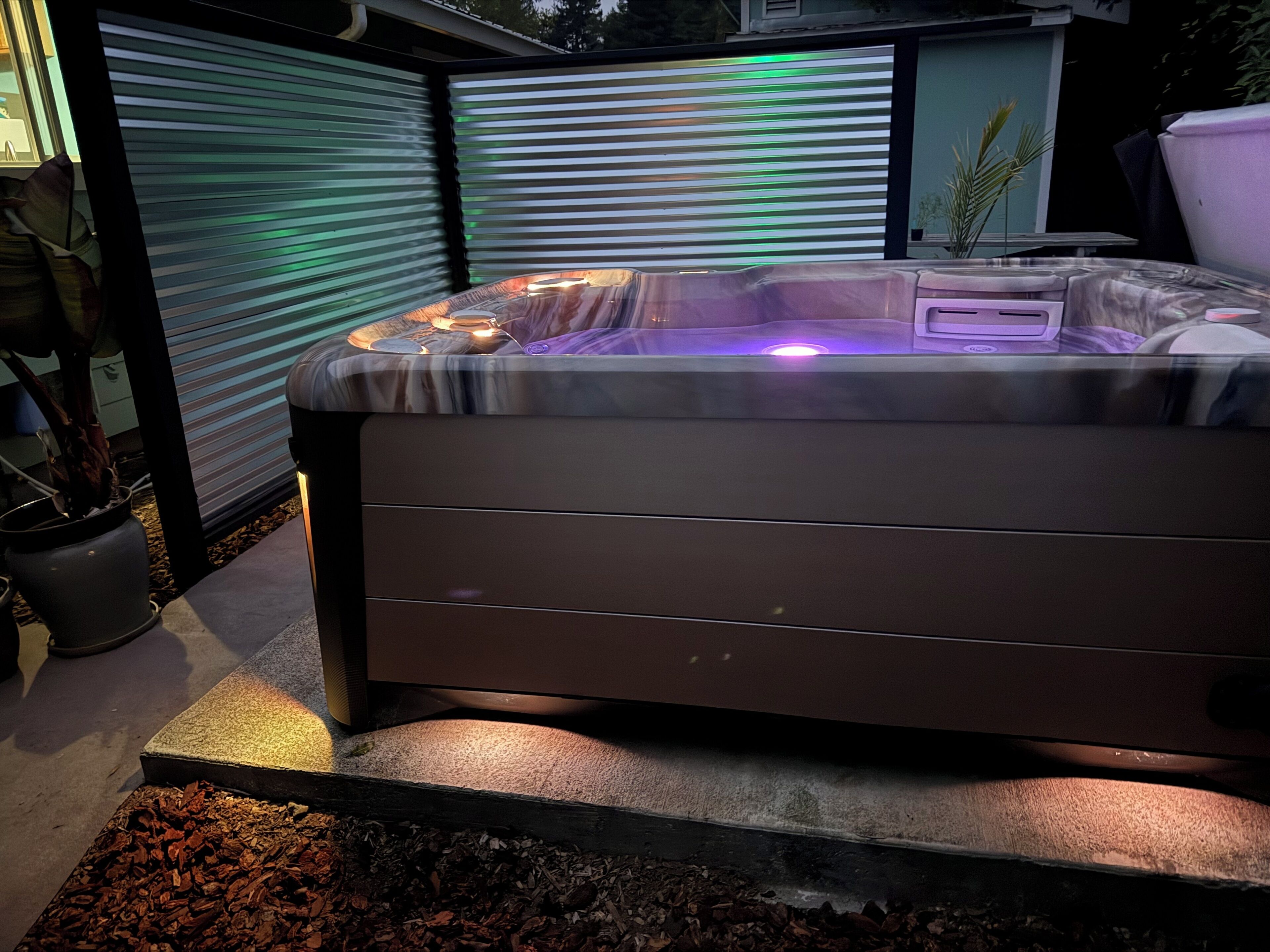 Un jacuzzi con tapa, rodeado por un patio con mantillo y plantas en macetas.