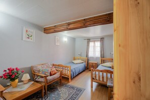 A cozy bedroom with a wooden bed, a wooden chair, a bedside table, and a small desk with a lamp.