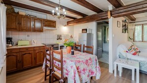 Une cuisine avec des meubles en bois, une table à manger recouverte d’une nappe à motifs floraux et un lustre.