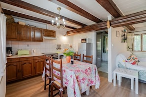 Une cuisine avec des meubles en bois, une table à manger recouverte d’une nappe à motifs floraux et un lustre.