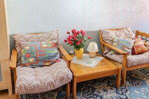 Ein gemütliches Zimmer mit zwei Holzsesseln, einem kleinen Tisch, einer Vase mit Blumen und einer Lampe.