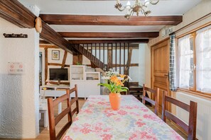 A dining area with a wooden table, chairs, a vase with flowers, a staircase, and a sign on the wall.