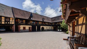 Une cour intérieure avec un bâtiment doté d’une façade traditionnelle à pans de bois, d’une tour horloge et d’une galerie couverte.