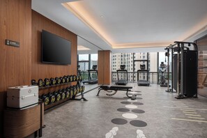 Un gimnasio moderno con equipo de ejercicio, un televisor y vistas a la ciudad.