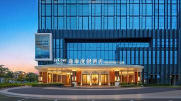 A modern hotel with a glass facade, a well-lit entrance, and a signboard advertising the hotel.