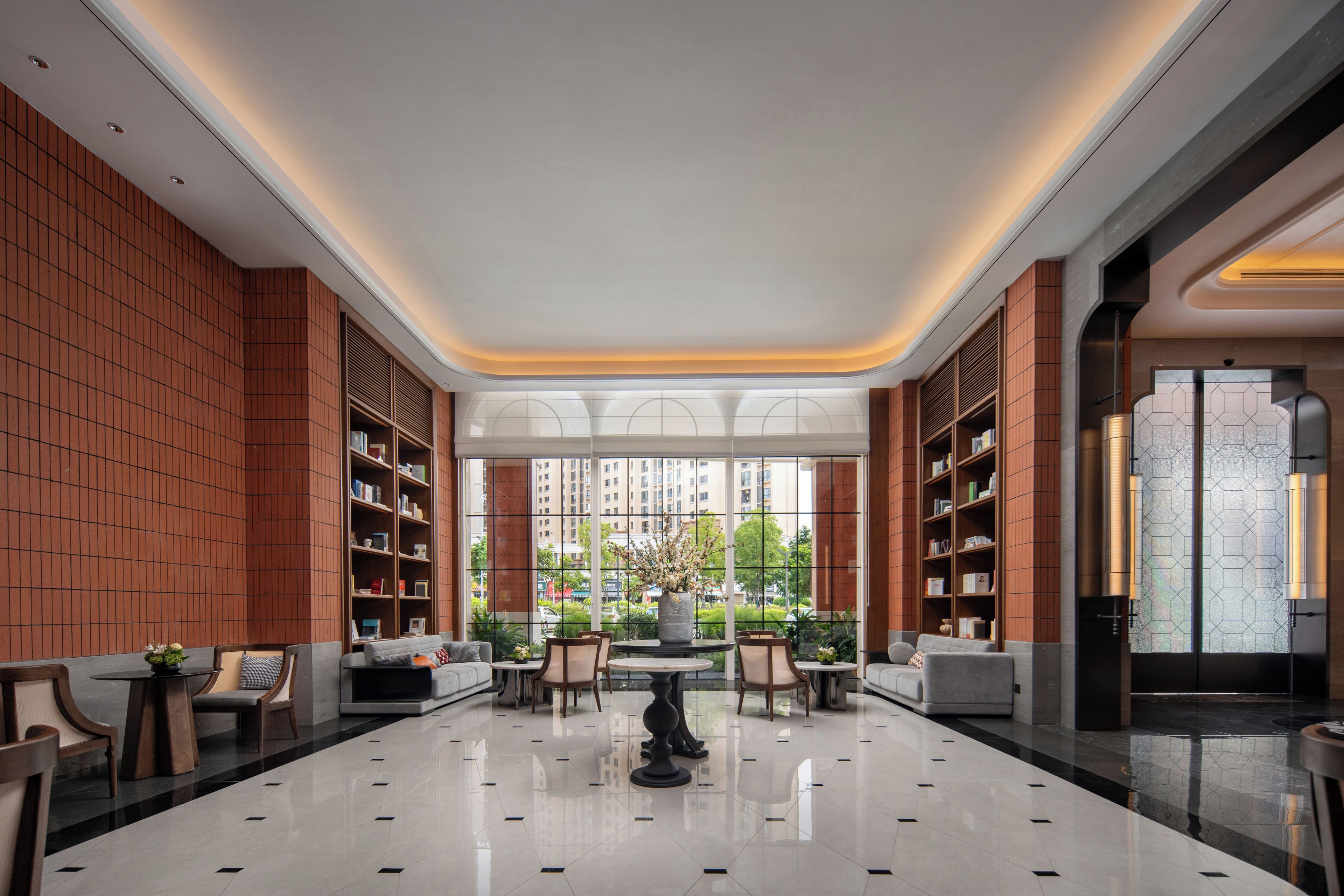 A spacious lobby with a high ceiling, large windows, and a central seating area with tables and chairs.
