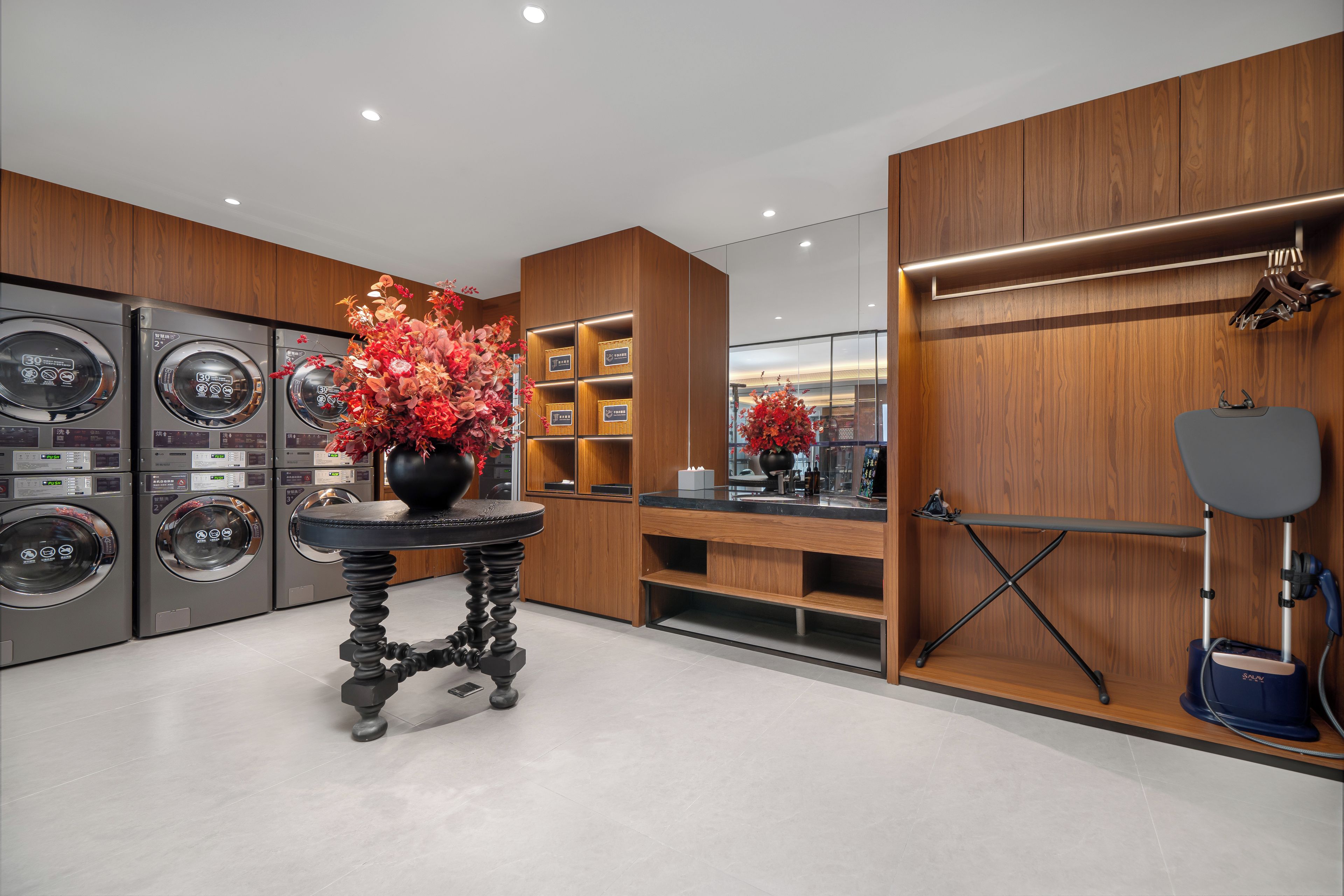 Un moderno cuarto de lavandería con varias lavadoras, un jarrón decorativo y un rincón para limpiar zapatos.