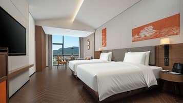 A hotel room with two beds, a TV, a desk, and a view of the mountains.