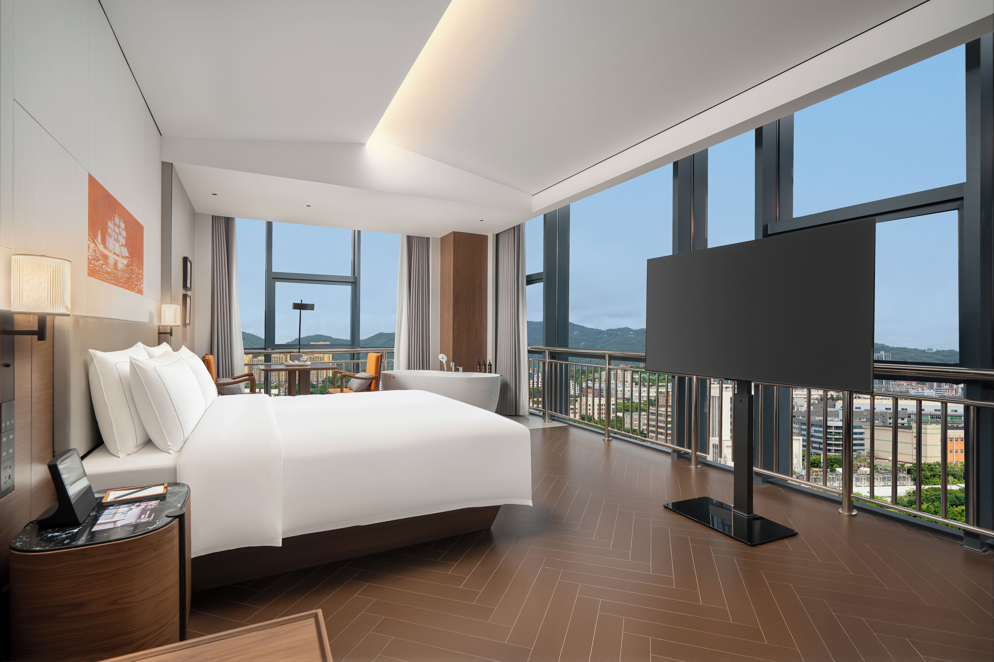 A modern hotel room with a large bed, a desk, a TV, and a balcony with a city view.