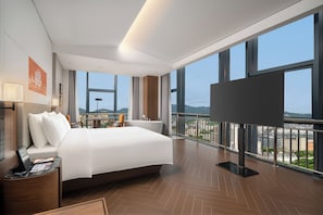 Ein modernes Hotelzimmer mit einem großen Bett, einem Schreibtisch, einem Fernseher und einem Balkon mit Blick auf die Stadt.