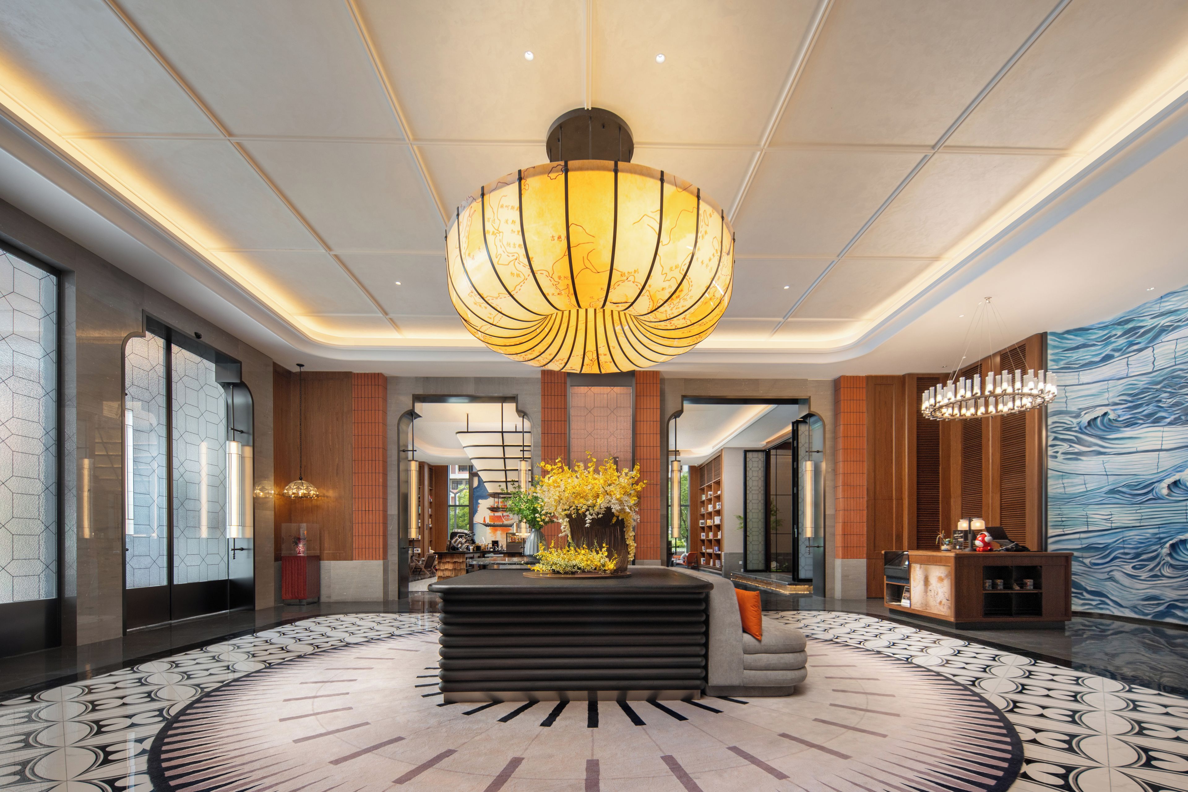 A modern lobby with a central seating area, a large chandelier, and a patterned floor.