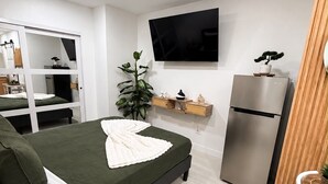 Une chambre moderne équipée d’un lit, d’un bureau, d’une télévision et d’un réfrigérateur.