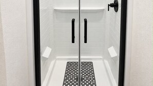 Une douche avec une porte en verre, une pomme de douche noire et un panneau de commande.
