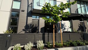 A modern two-story building with a balcony, large windows, and a landscaped front yard. - 3-bedroom townhome with roof top patio - Gyro Beach across the street (Kelowna)