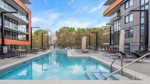 A swimming pool with lounge chairs and tables, surrounded by modern buildings. - 3-bedroom townhome with roof top patio - Gyro Beach across the street (Kelowna)