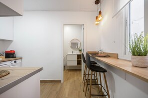 Een moderne keuken met een vaatwasser, een koffieapparaat en een eethoek met een houten tafel en barkrukken.