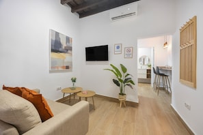 Een woonkamer met een bank, een televisie, een kleine tafel met een plant en een eethoek met stoelen.