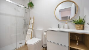 Ein modernes Badezimmer mit Duschkabine aus Glas, Toilette, Waschbecken mit Spiegel und einer kleinen Pflanze auf der Ablagefläche.