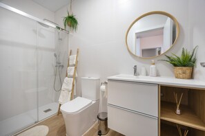 Een moderne badkamer met een douchecabine van glas, toilet, wastafel met spiegel en een kleine plant op het aanrecht.