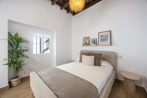 Een slaapkamer met een bed, een nachtkastje, een potplant en een raam.