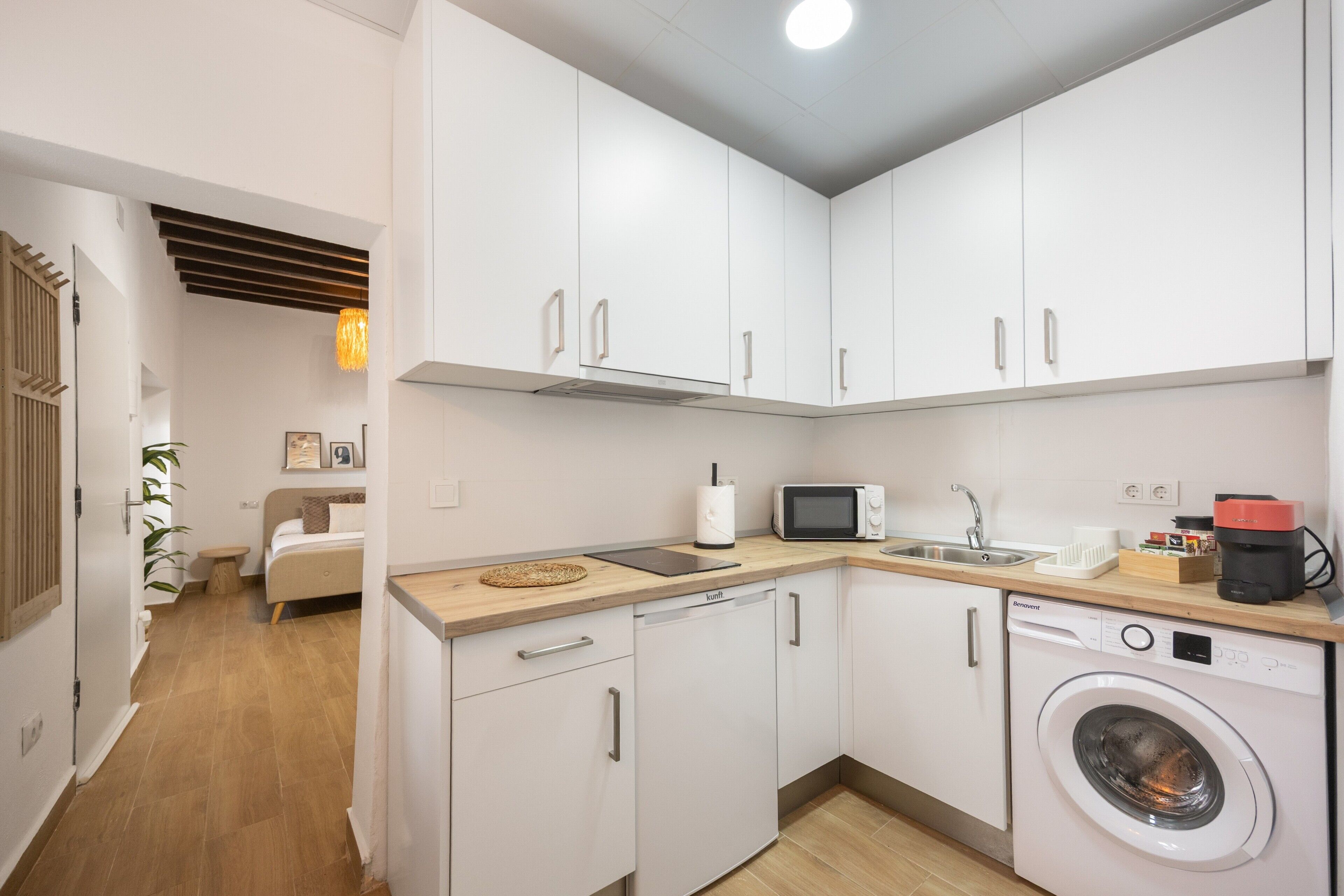 A compact kitchen with white cabinets, a microwave, a coffee maker, and a washing machine.