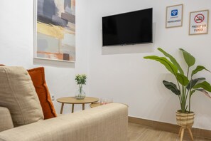 Una sala de estar moderna con un televisor de pantalla plana montado en la pared, una pequeña mesa redonda con un florero y una planta grande en maceta.