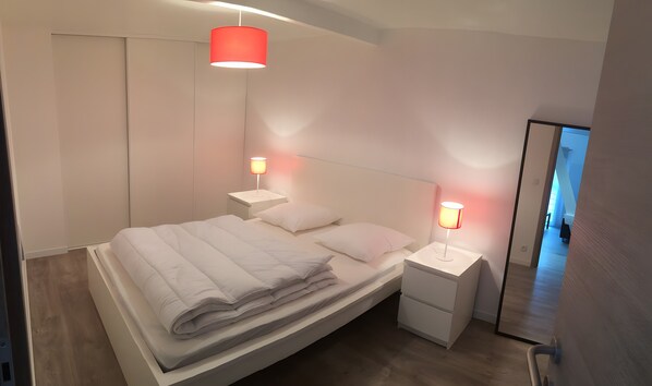 Un dormitorio moderno con cama, mesitas de noche y espejo.