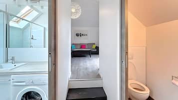 Un baño moderno con inodoro blanco, lavadora y cabina de ducha de vidrio.