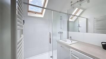 A modern bathroom with a skylight, a glass shower enclosure, a sink, and a washing machine.