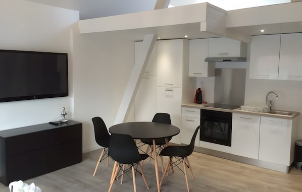 Cocina moderna con armarios blancos, una mesa de comedor negra con cuatro sillas y un horno empotrado.